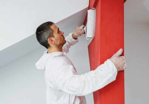 A man in a white uniform with a roller in his hand paints the ceiling white at home