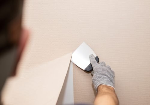 Man hand tear off old light wallpaper from wall.Preparing for home repair work.removing Wallpaper
