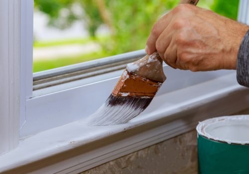 Painting a wooden window paint with paintbrush while painting window trim