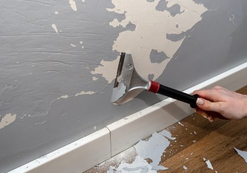 Removing silicone paint from a wall damaged by dog claws using a paint and adhesives scraper.