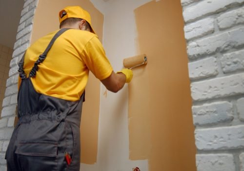 Worker painting wall with paint roller.